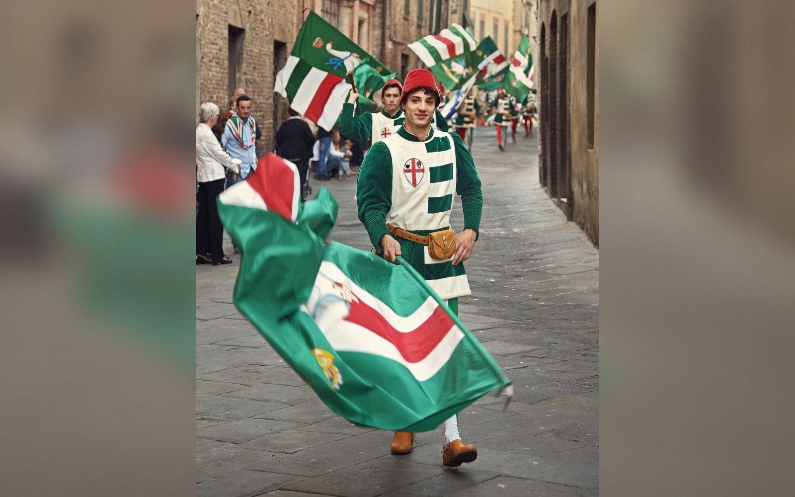 Flag bearers in medieval costume parade through a narrow stone street