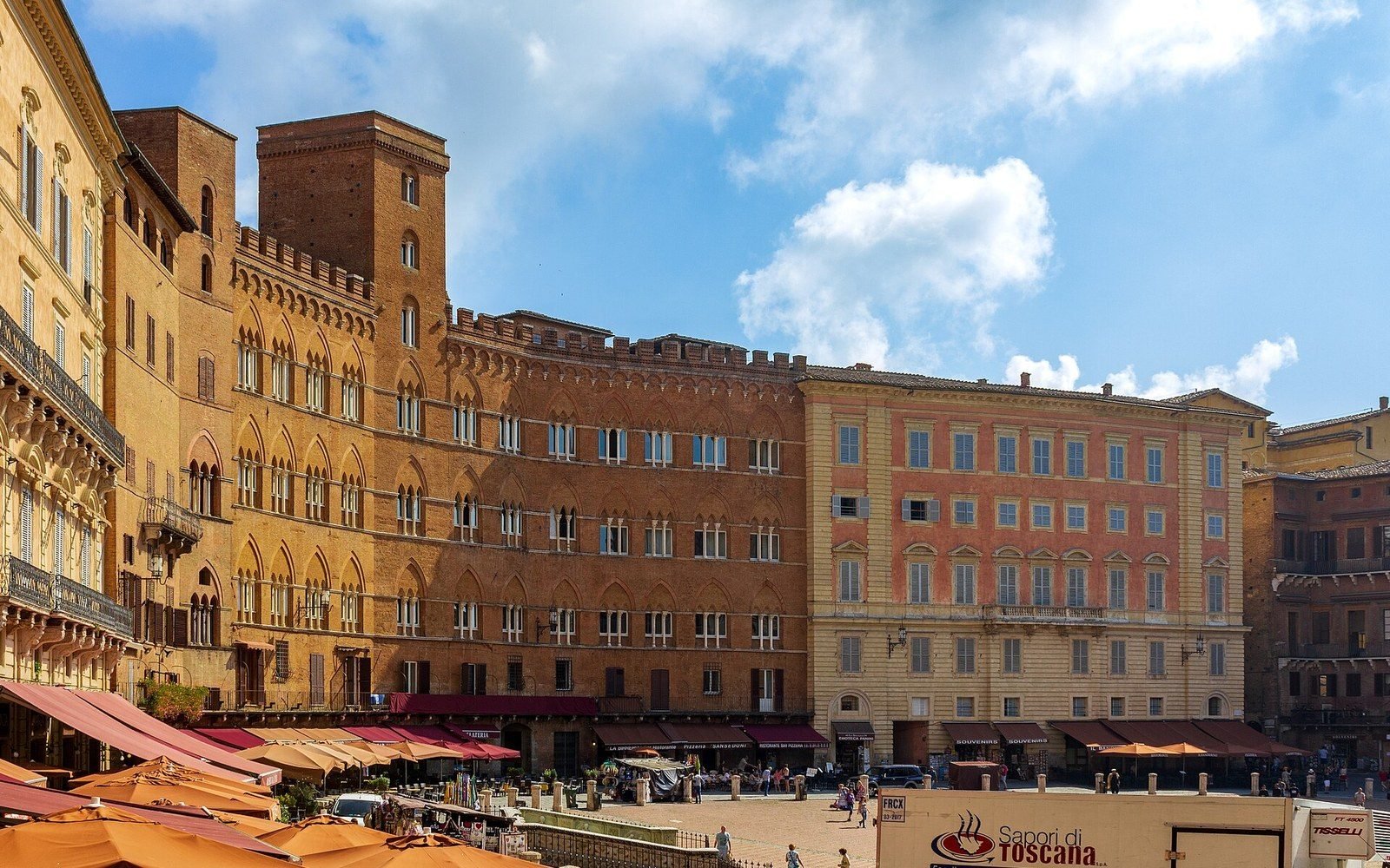 Medieval brick buildings with battlements line the Piazza del Campo, cafe umbrellas below